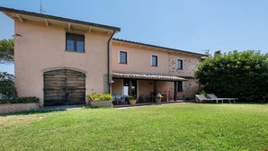 A two-story building with a large arched entrance, a covered porch, and a small garden area with outdoor furniture. - Room 'Among the Olive Trees and the View' with Mountain Views, Private Garden, and Wi-Fi (Orvieto)