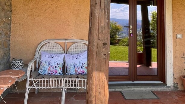 Un espacio de estar al aire libre cubierto con mesa y sillas de madera, una planta en maceta con flores y vistas al paisaje a través de un ventanal.