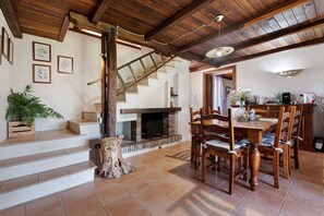 Un interior rústico con una escalera de madera, una chimenea, un comedor con sillas de madera y un techo con vigas a la vista.