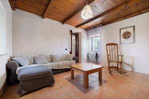 Una habitación con techo de madera, un sofá, una mesa, un sillón mecedora y un cuadro enmarcado en la pared.