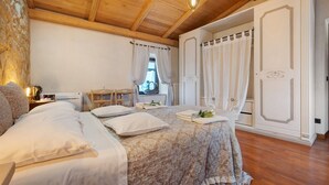 Un dormitorio con techo de madera, una cama con colcha estampada, una mesita de noche con lámpara y una ventana con cortinas.