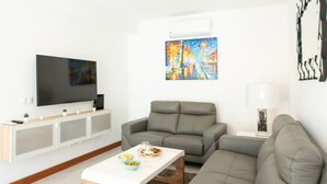 A modern living room with a flat-screen TV, a grey sofa, a coffee table with food and drinks, and a colorful painting on the wall. - Vacation Home 'Leize Con Piscina' with Sea View, Wi-Fi and Air Conditioning (Yaiza)