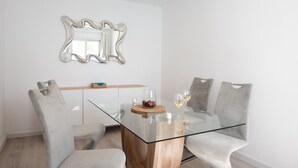 A modern dining area with a glass-top table, cushioned chairs, a decorative mirror, and a wooden cabinet. - Vacation Home 'Leize Con Piscina' with Sea View, Wi-Fi and Air Conditioning (Yaiza)