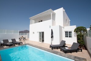 Um edifício moderno e branco com piscina, espreguiçadeiras e um terraço coberto.