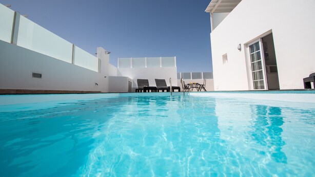 A clear blue pool with lounge chairs and a white building in the background. - Vacation Home 'Leize Con Piscina' with Sea View, Wi-Fi and Air Conditioning (Yaiza)