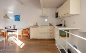 A modern kitchen with white cabinetry, a wooden dining table with chairs, and a hanging pendant light. - The Abode of the Poets, TerreMarine (Lerici)