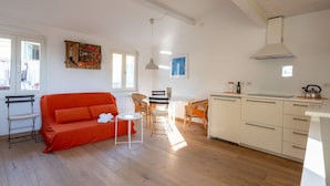 A bright living room with a red sofa, a small round table, and a dining area with chairs. There is a kitchen with white cabinets and a stove. - The Abode of the Poets, TerreMarine (Lerici)