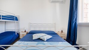 A single bed with a headboard, a window with curtains, an air conditioning unit, and a bedside table with a lamp. - Apartment 'Marittima' with Balcony, Wi-Fi and Air Conditioning (Torre Canne)