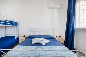 Un lit simple avec une tête de lit, une fenêtre avec des rideaux, un appareil de climatisation et une table de chevet avec une lampe.