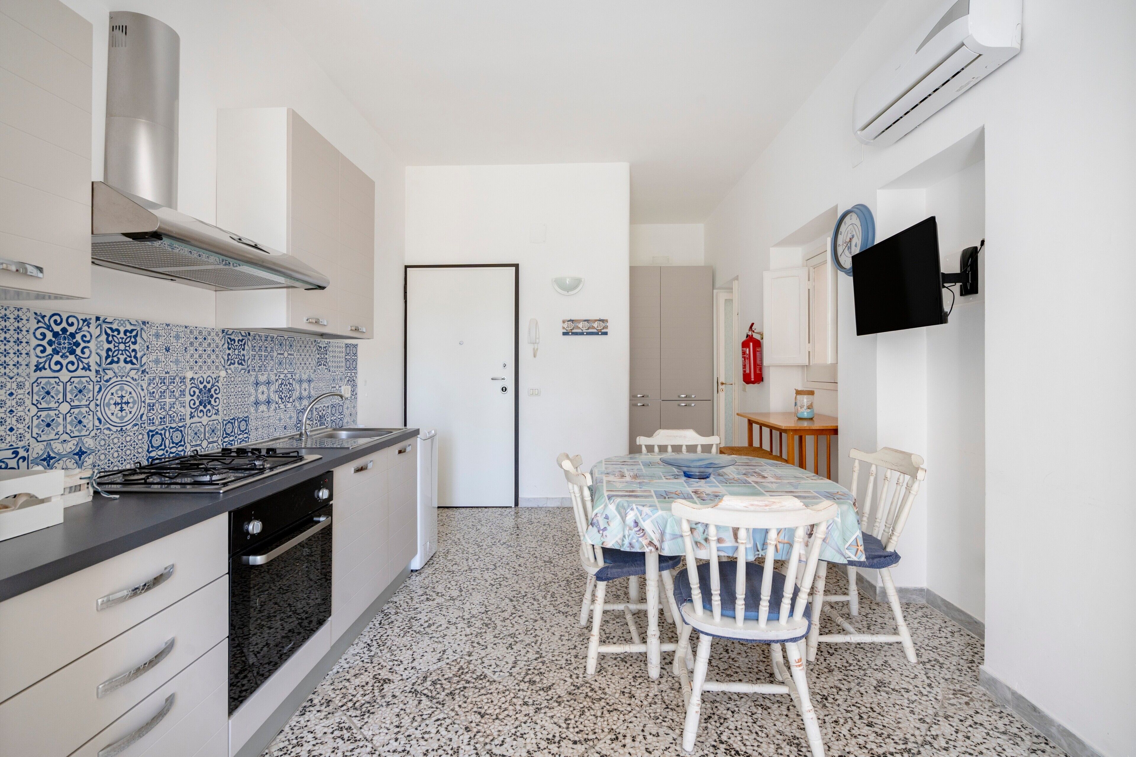 A kitchen with a gas stove, oven, and stainless steel range hood. There is a dining area with a table and chairs.
