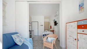 A compact living space with a blue sofa, a wicker chair, a small dining table, and a white cabinet. - Apartment 'Marittima' with Balcony, Wi-Fi and Air Conditioning (Torre Canne)
