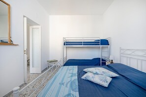 Ein Schlafzimmer mit Etagenbetten, einem kleinen Hocker, einem Nachttisch mit Lampe und einer Tür zu einem anderen Raum.
