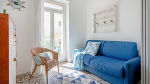 A room with a blue sofa, a wicker chair, a nautical-themed wall decoration, and a white shelf with plants. - Apartment 'Marittima' with Balcony, Wi-Fi and Air Conditioning (Torre Canne)
