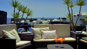 A rooftop terrace with wicker furniture, cushions, and a table with a drink.