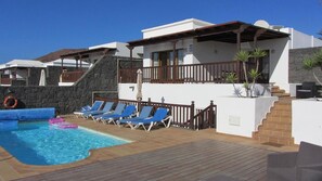 A pool area with lounge chairs, a stone wall, and a staircase leading to a covered deck. - Vacation 'Casa Laura' with Heatable Pool, Sea View, Wi-Fi and Air Conditioning (Playa Blanca)