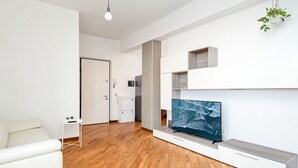 A modern living room with a flat-screen TV, white furniture, and a wooden floor.