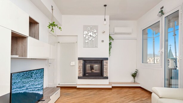 A modern living room with a fireplace, a flat-screen TV, and a large window offering a city view.