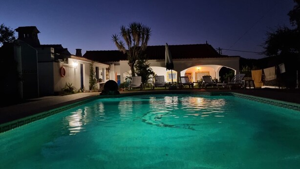 A swimming pool with lounge chairs and a covered area, surrounded by buildings.