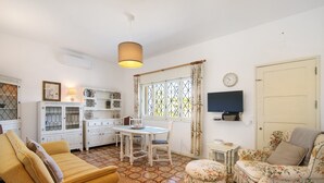 A living room with a sofa, a dining table, a TV, and a window with curtains.