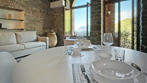 A dining area with a round table set for two, a stone wall, and a view of the outdoors. - Blue Stone, Marine Lands (Corniglia)
