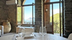 A dining table set with white plates, bowls, and wine glasses, overlooking a mountainous landscape through large windows. - Blue Stone, Marine Lands (Corniglia)