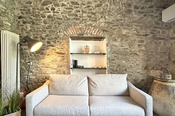 A cozy room with a stone wall, a white sofa, a lamp, and a shelf with decorative items.