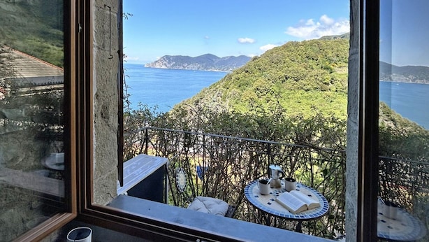 A balcony with a view of the sea and hills, a table with books, and a small table with a cup and saucer. - Blue Stone, Marine Lands (Corniglia)