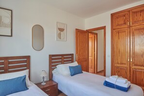 A bedroom with two beds, wooden wardrobes, a bedside table with a lamp, and artwork on the wall. - Vacation 'Maria Del Mar' with Mountain View, Private Pool and Wi-Fi (Playa Blanca)