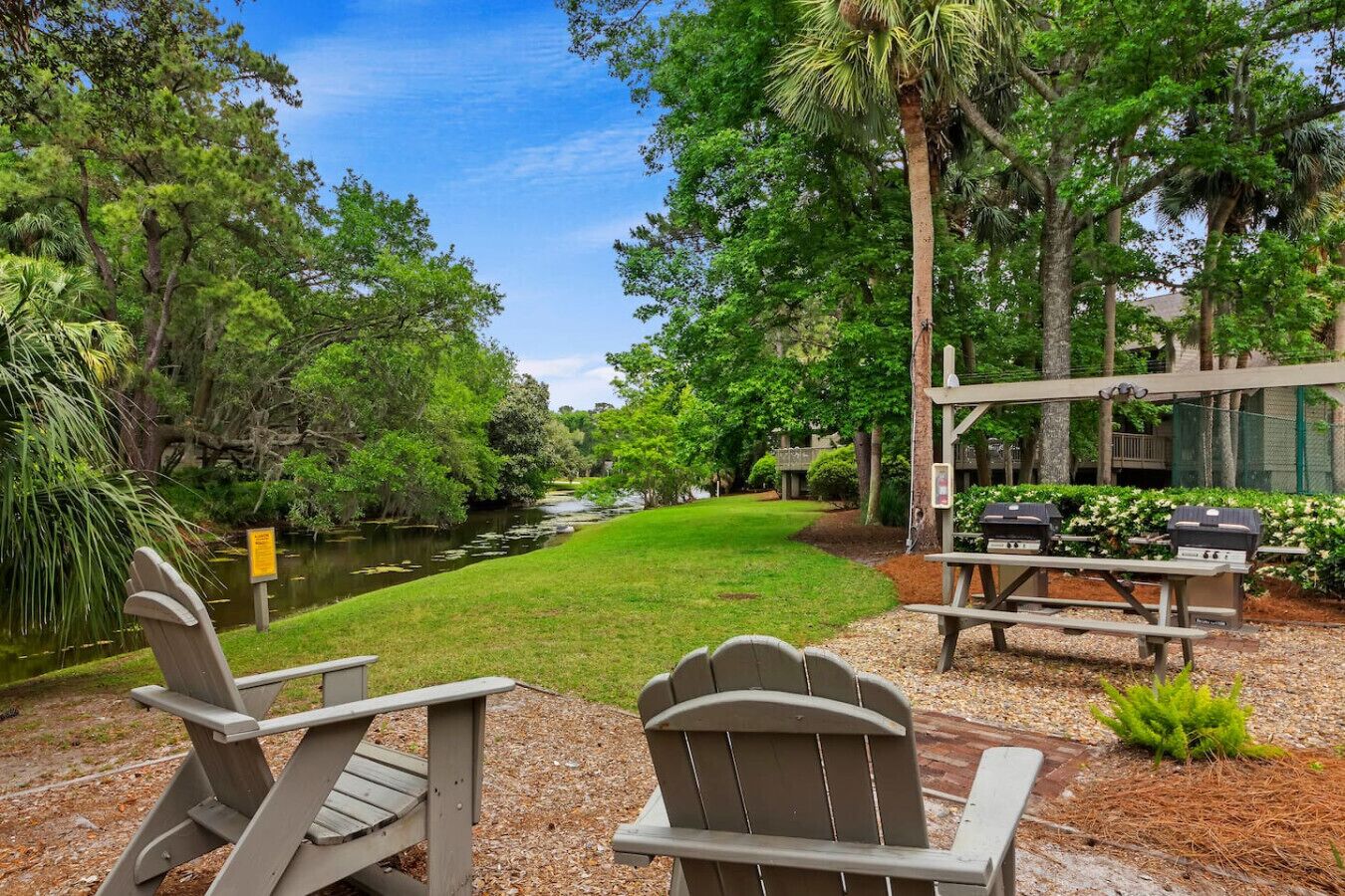 A serene outdoor area with a grassy lawn, a small pond, and a barbecue setup.