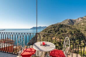 A balcony with a round table and red cushions, overlooking a coastal landscape with hills and a clear blue sea. - Rossi Tramonti 1, Terre Marine (Corniglia)