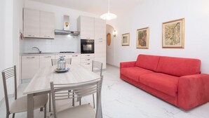 Una cocina moderna con armarios blancos, una mesa de comedor con sillas y un sofá rojo.
