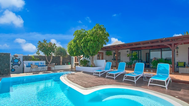Une piscine avec des chaises longues, une terrasse en bois et un espace salon abrité.