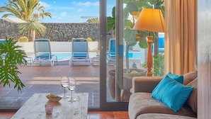 Un espace aménagé au bord de la piscine, avec des chaises longues, une table sur laquelle se trouve un saladier rempli de fruits et des verres, ainsi qu’un canapé agrémenté d’un coussin bleu.