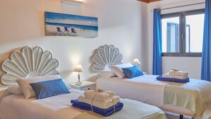Une chambre d’hôtel avec deux lits, un tableau représentant une scène de plage et une fenêtre avec des rideaux.