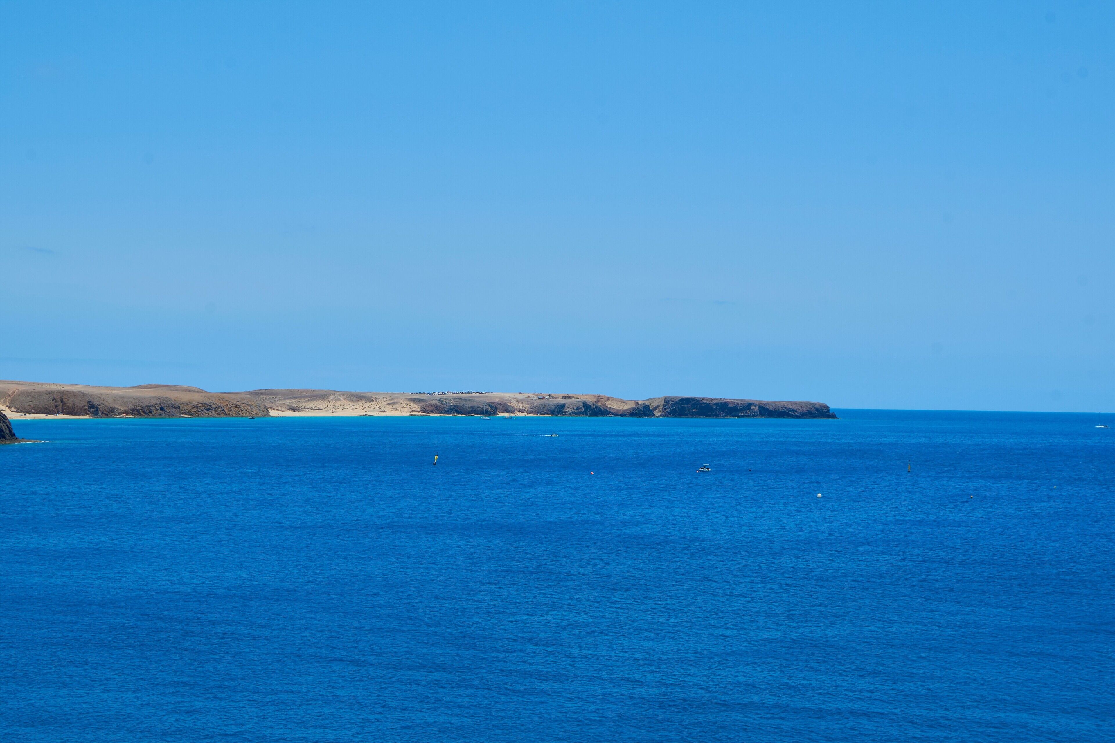 A coastal landscape with clear blue waters, distant rocky formations, and a few boats.