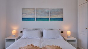 Een net opgemaakt bed met witte lakens, twee bedlampjes en een set handdoeken op het bed.