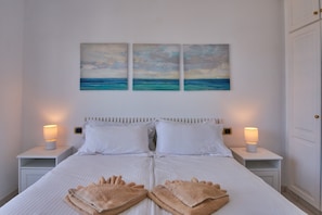 A neatly made bed with white linens, two bedside lamps, and a set of towels on the bed.