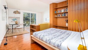 Un dormitorio moderno con una cama grande, estanterías de madera, un escritorio y un área de comedor con vistas a zonas verdes.