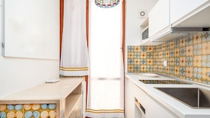 Una cocina compacta con encimera blanca, un lavamanos y suelo de baldosas estampadas.