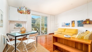 Una sala de estar moderna con una mesa de comedor de vidrio, sillas blancas, un sofá amarillo y obras de arte en las paredes.