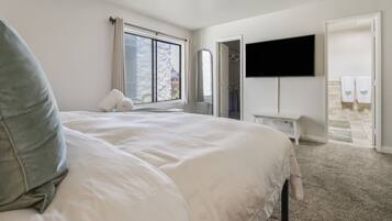 Ein Hotelzimmer mit einem großen Bett, einem flachbildfernseher an der Wand, einem begehbaren Kleiderschrank und einem Badezimmer mit Dusche und Handtüchern.