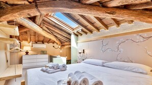 A bedroom with a wooden ceiling, a bed with white linens, a bedside table, and a wall with a floral design. - Magnolia, Welcome Way (Lerici)