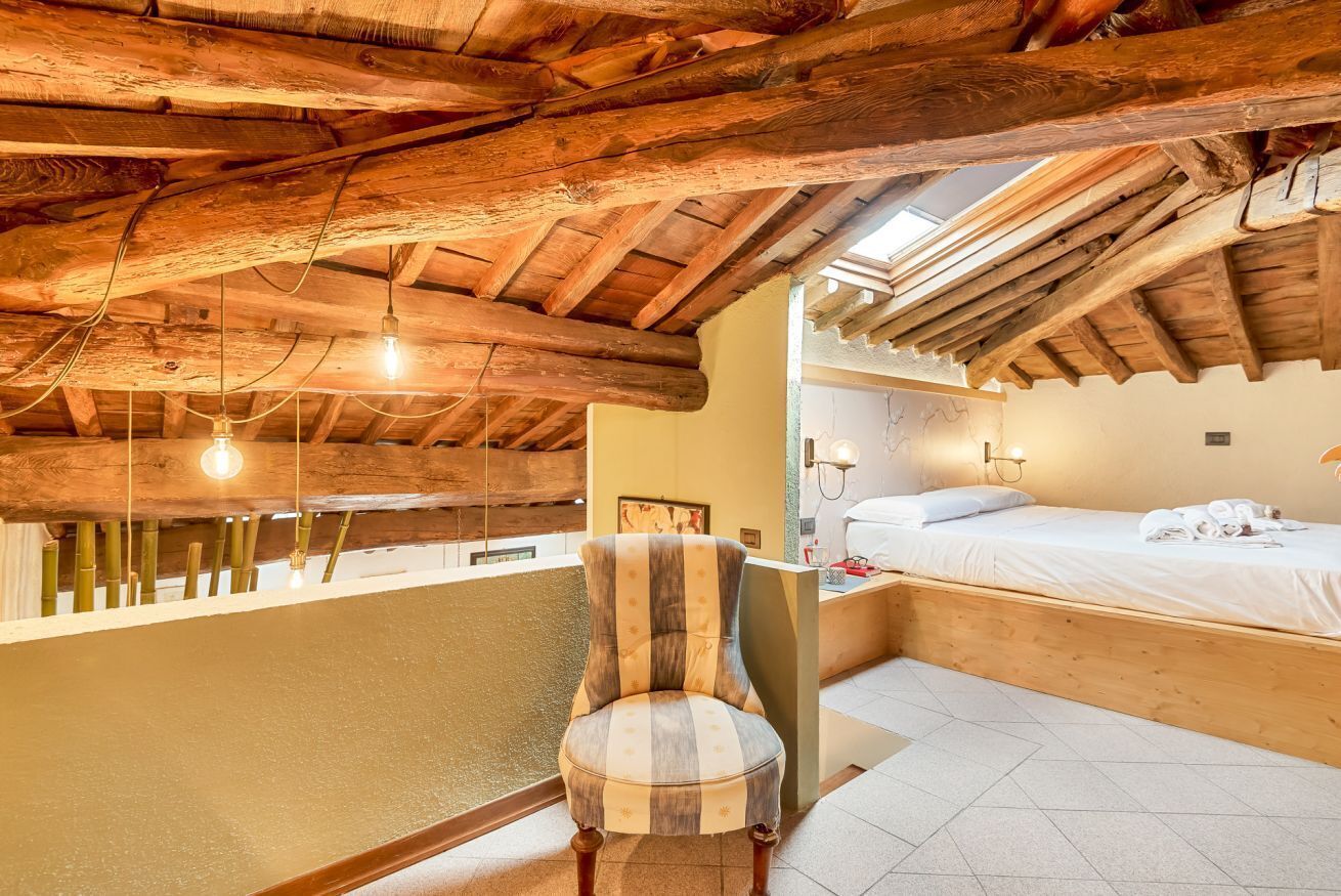 Eine rustikale Holzbalkendecke, ein gestreifter Sessel, ein Bett mit weißer Bettwäsche und ein kleiner Nachttisch.