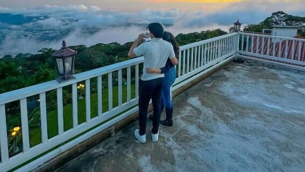 Un couple sur une terrasse en toit, avec vue sur le paysage urbain illuminé par le coucher du soleil.