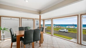A dining area with a wooden table and black chairs, large windows with a view of the sea and a road.