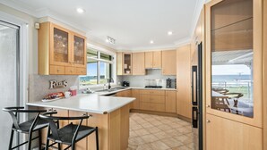 A modern kitchen with wooden cabinets, a central island, and a view of the sea.