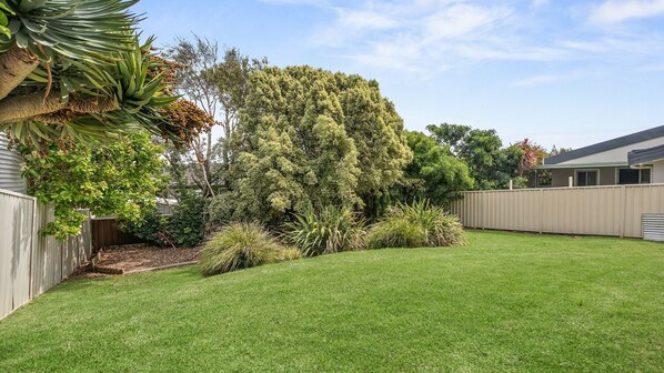 A backyard with a well-maintained lawn, a tall tree, and a wooden fence.