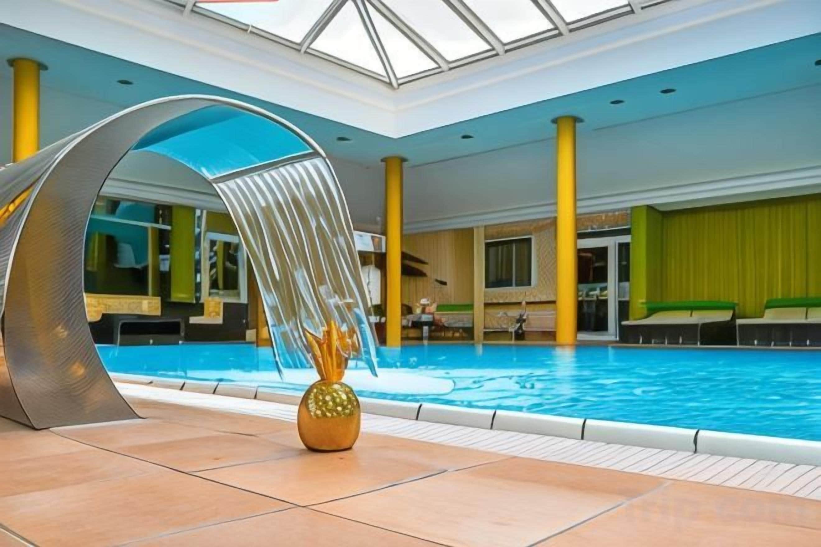 Ein überdachter Innenpool mit einem Wasserspiel und einer Sitzecke mit grünen Kissen.