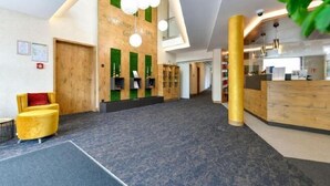 Moderni hotellin aula, jossa on vastaanottotiski, puuelementtejä ja vihreä seinä, jossa on hyllyjä.