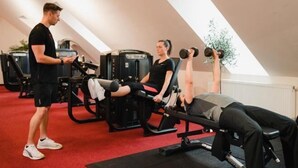 Kuntosali, jossa on kuntoilulaitteita, punainen matto ja henkilö, joka käyttää yhtä laitteista.